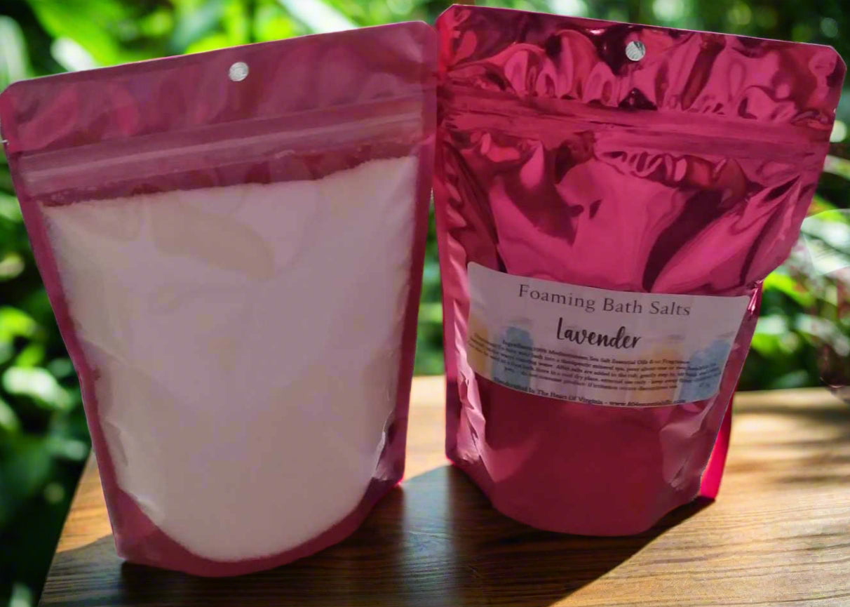 Two pink packages of foaming bath salts labeled 'Lavender' on a wooden surface with a blurred green background.