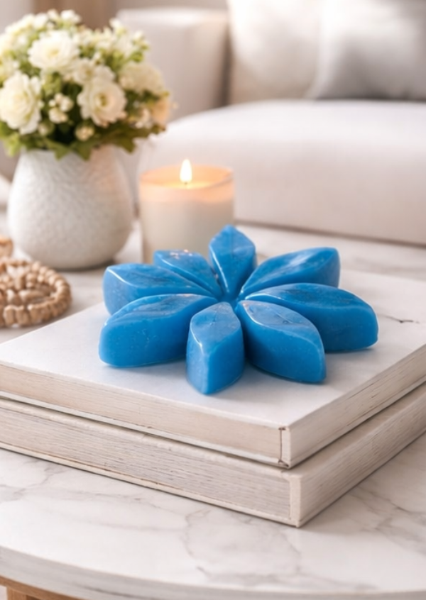 Collage of blue and green flower-shaped candles on a table with a white couch and flowers in the background.