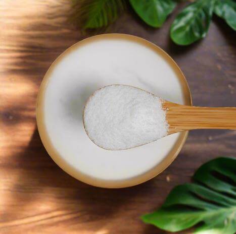 Bowl of white powder with a wooden spoon on a wooden surface with green leaves.
