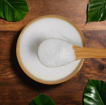 Bowl of white powder with a wooden spoon on a wooden surface with green leaves.