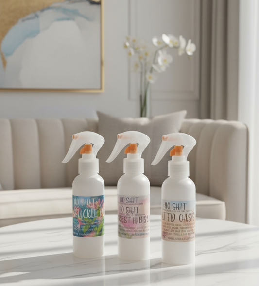 Three spray bottles on a marble table with a neutral-colored wall and abstract art in the background.