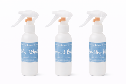 Three white spray room and linen spray bottles with blue labels on a white background
